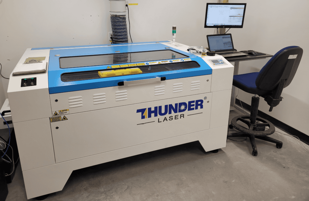 A CO2 laser engraver in operation, with a checklist and computer screen nearby