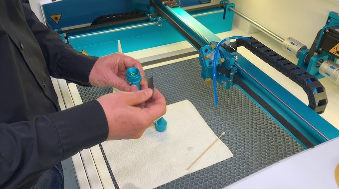 A person setting up a CO2 laser engraver, surrounded by tools and materials, with the machine's components laid out on a table for assembly