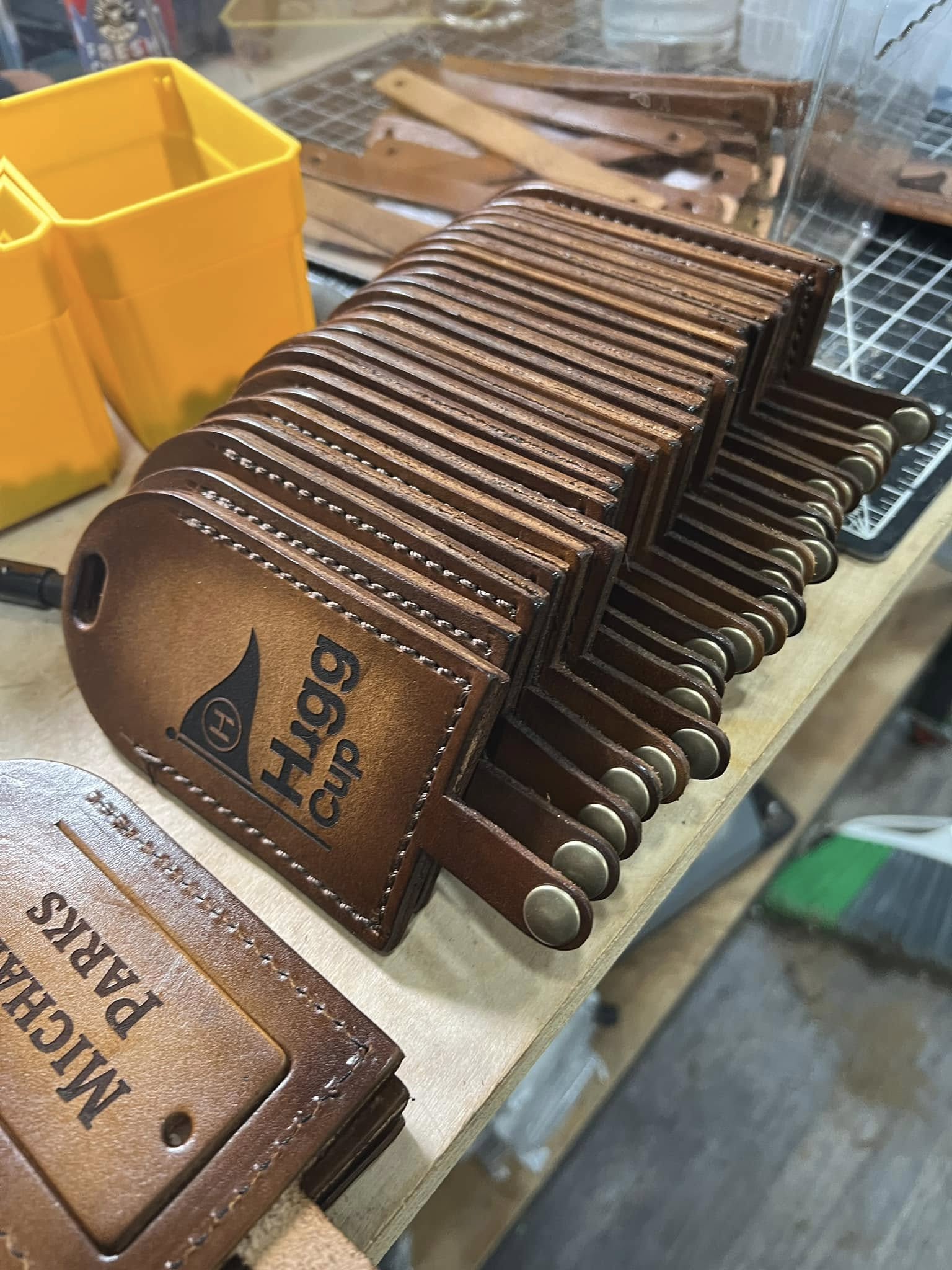 A leather piece sits on a workbench, surrounded by cleaning supplies and a laser engraving machine. The engraving on the leather shows intricate details