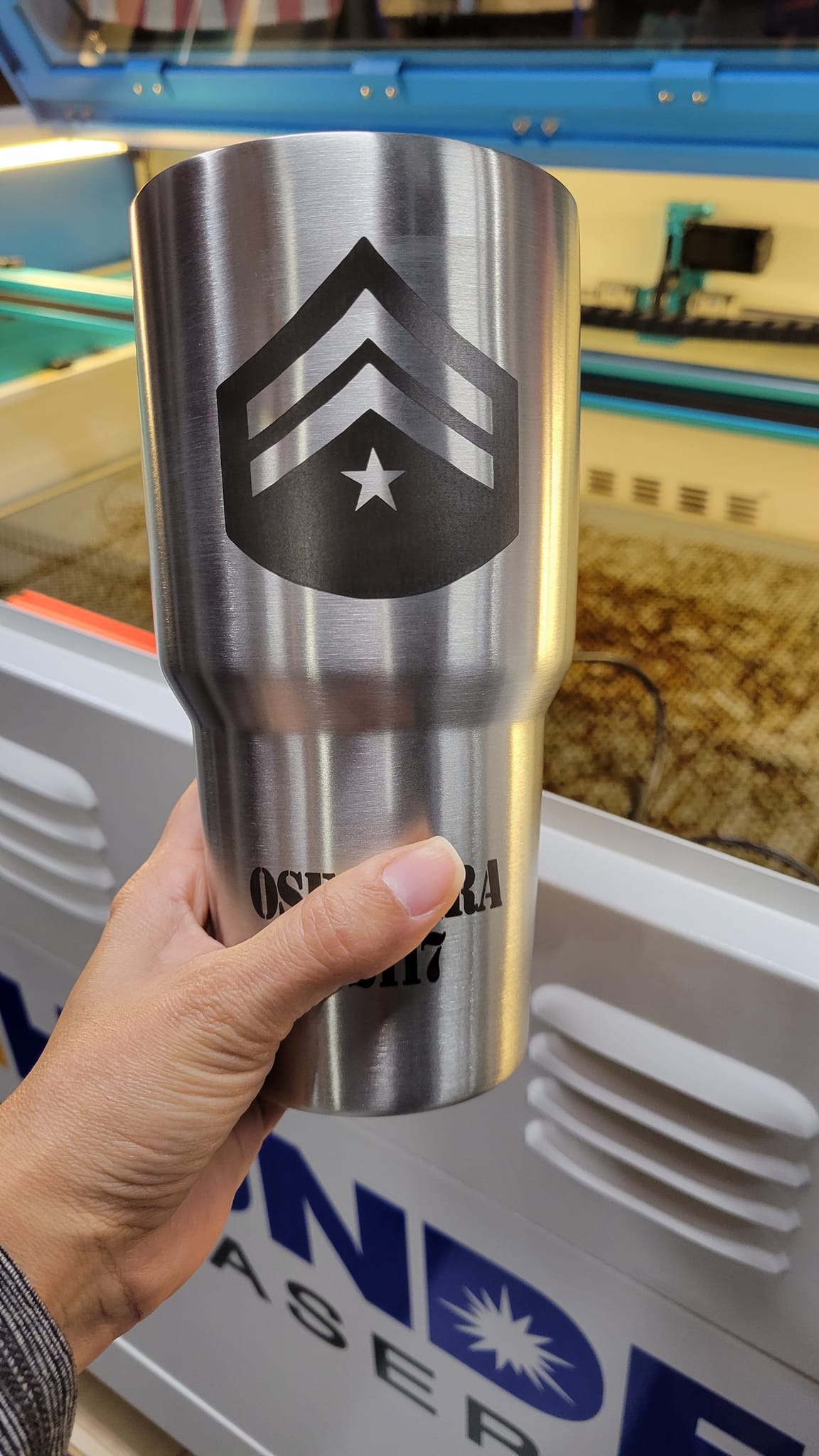 A laser engraver etches intricate designs onto a stainless steel tumbler, emitting a bright beam of light as it carefully crafts the pattern